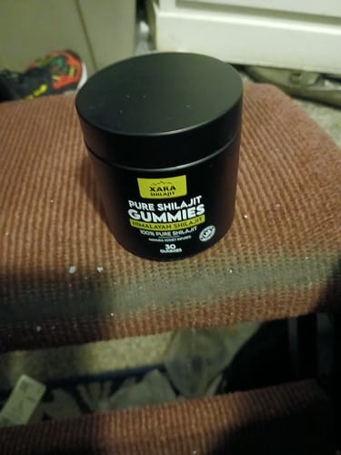 Customer's black container of XARA SHILAJIT Pure Shilajit Gummies sitting on a textured brown surface.