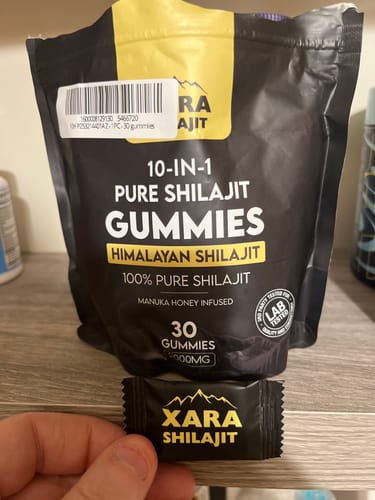 Customer holding a single wrapped XARA Shilajit Gummy in front of the black and yellow product pouch.