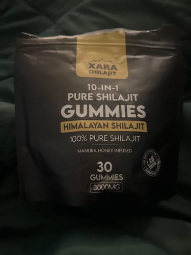 Customer's black pouch of XARA SHILAJIT Pure Shilajit Gummies resting on a green surface.