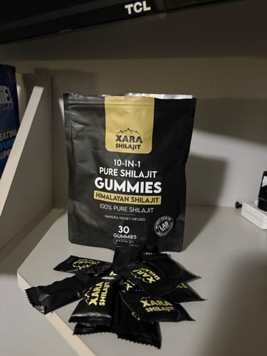 Customer's black pouch of XARA SHILAJIT Pure Shilajit Gummies on a shelf with several individual gummies in front.