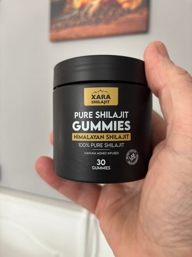 Reviewer's hand holding a black tub of Pure Shilajit Gummies.