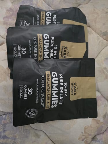 Reviewer's three black packages of XARA SHILAJIT Pure Shilajit Gummies lying on a quilted surface.